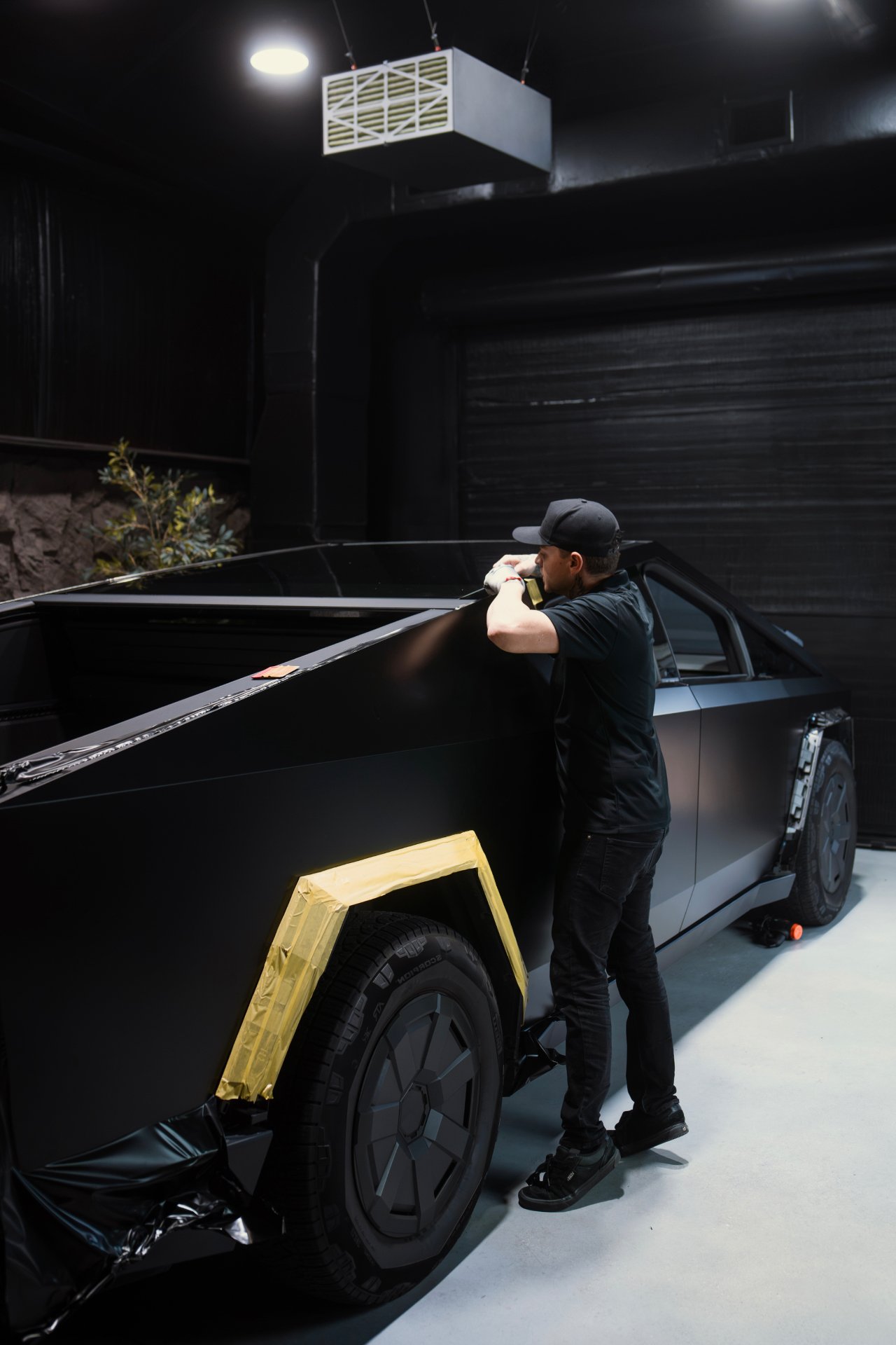 Installer hand-applying matte black vinyl wrap to a truck bed in the dark installation bay at High Society Customs